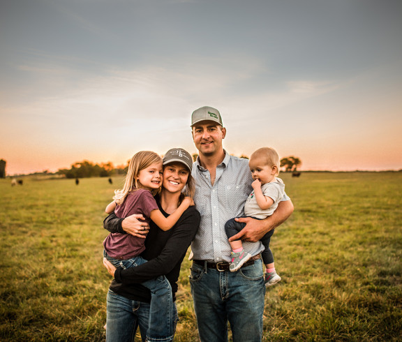 man, woman, little girl and baby stand in field with cows